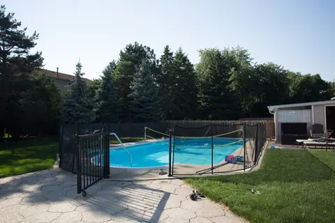 A backyard inground pool with a safety fence around the deck